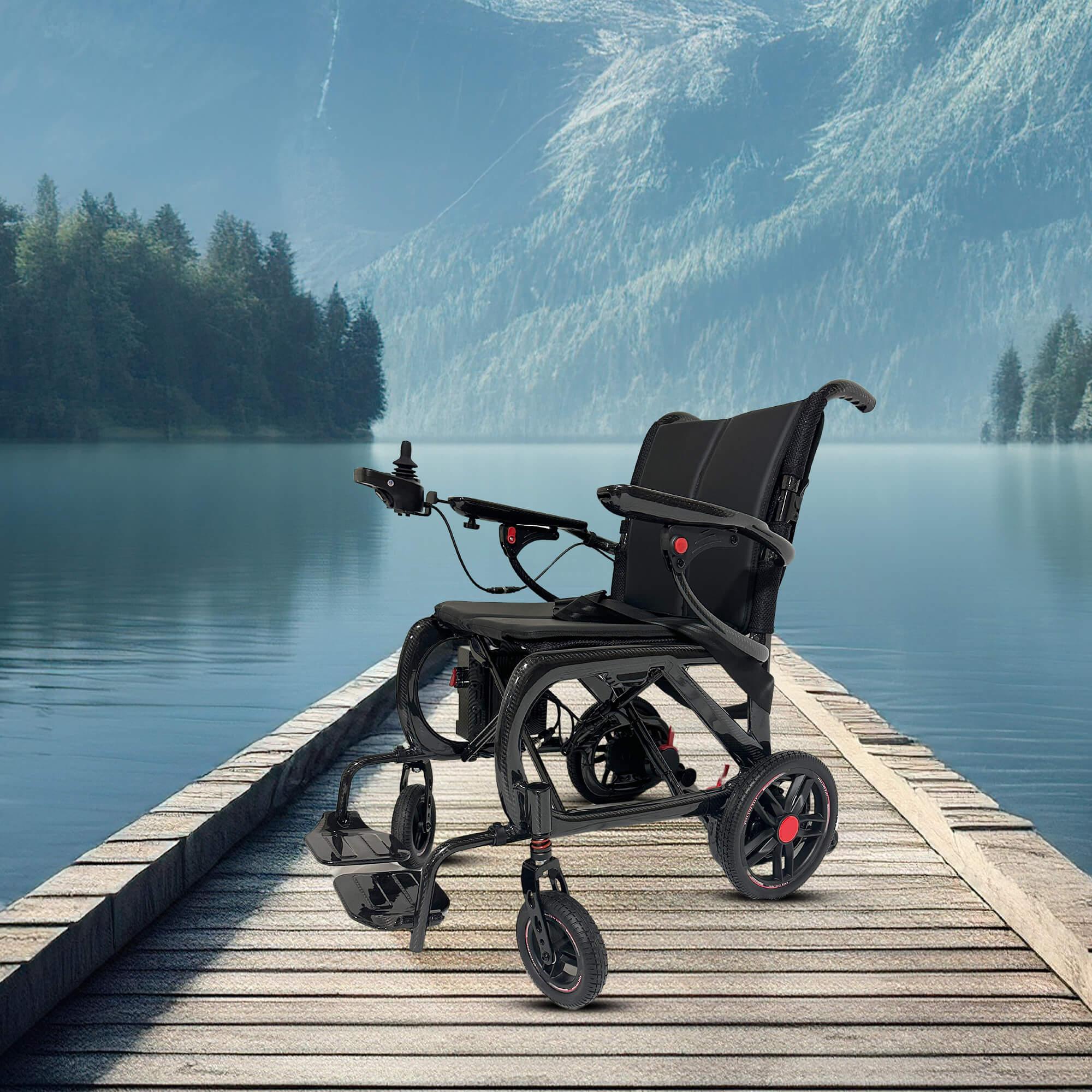 The MLS-20 Malisa Carbon Fiber Electric Wheelchair by Malisa Mobility sits empty on a wooden dock overlooking a calm lake, with forested mountains in the background beneath a clear sky.
